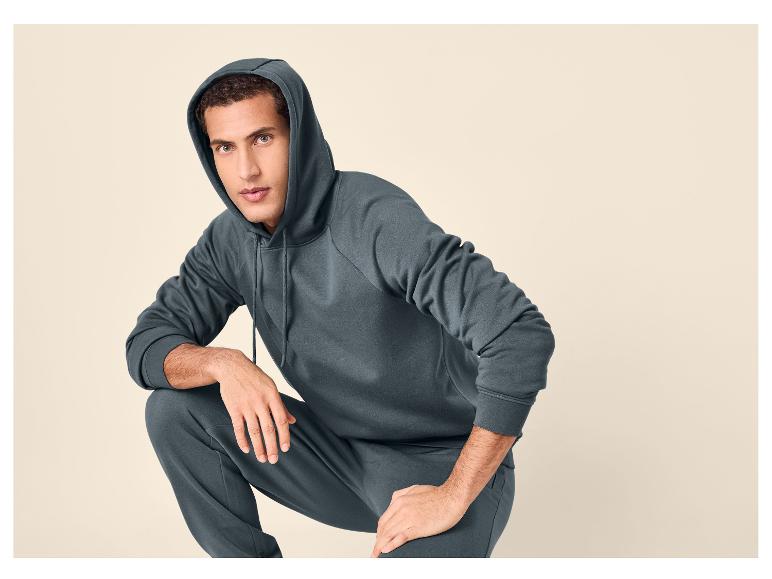 Homme en survêtement gris foncé, sweat à capuche et pantalon de jogging, accroupi.