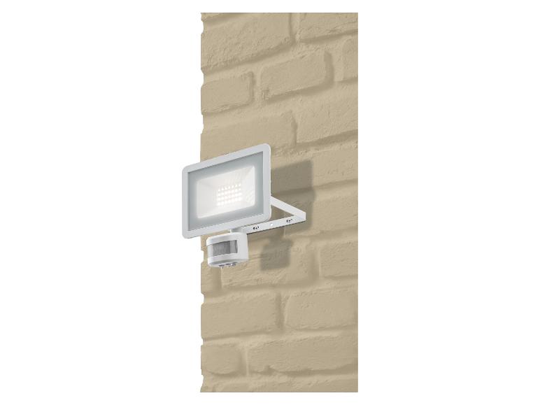 Projecteur LED blanc avec détecteur de mouvement sur un mur de briques beige.