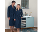 Couple en peignoirs bleu marine debout dans une salle de bain près d'un lavabo.