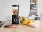 Mixeur noir avec des fruits coupés sur un comptoir de cuisine en bois clair.