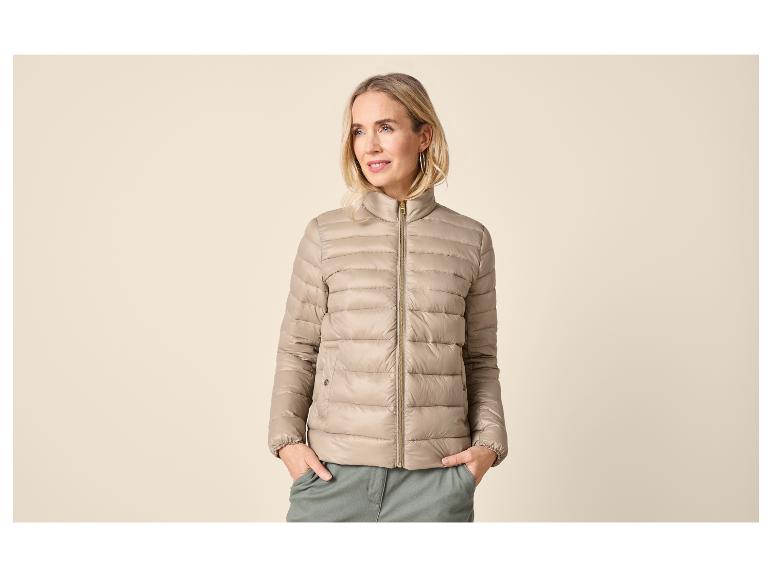 Femme portant une doudoune beige et un pantalon vert, les mains dans les poches.