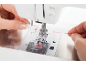 Femme enfilant manuellement du fil rouge dans une machine à coudre.