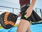 Femme sur un court de padel avec une raquette et une balle dans sa poche, vêtue d'un haut de sport et d'une jupe.