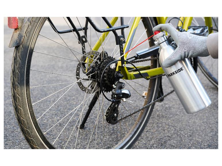 Main gantée lubrifiant une chaîne de vélo avec un flacon pulvérisateur.