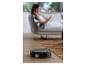 Robot aspirateur nettoyant un parquet pendant qu'une femme se détend sur le canapé.