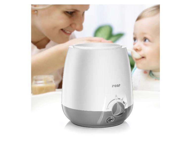 Chauffe-biberon blanc et gris avec une mère souriante nourrissant un bébé en arrière-plan.