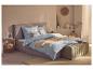 Chambre avec parure de lit à carreaux bleu clair, cadre de lit et pouf marron clair, tapis clair.
