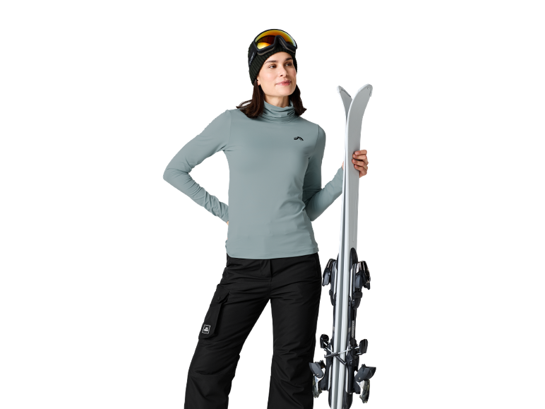 Femme en tenue de ski avec skis, lunettes de ski et bonnet.