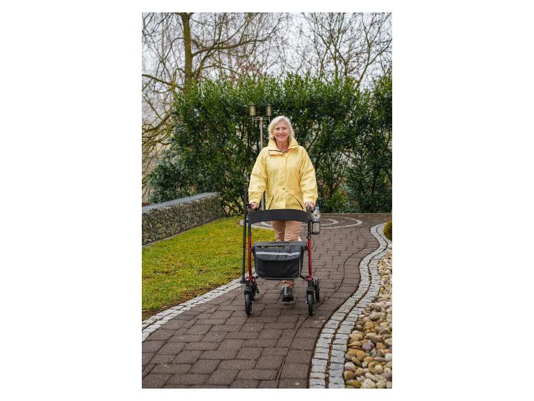 Femme âgée en veste jaune marchant avec un déambulateur sur un chemin pavé.