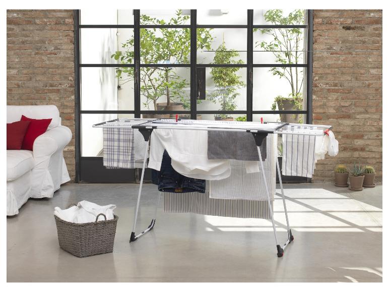 Séchoir à linge avec vêtements séchant dans un salon lumineux avec canapé et plantes.
