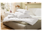 Oreillers et couettes blancs matelassés sur un lit.