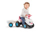 Un enfant conduit un tracteur Falk rose avec une remorque.
