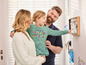 Une famille regarde des photos et des dessins accrochés au mur.