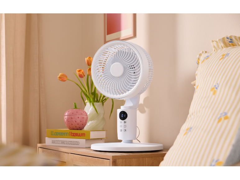 Ventilateur de table blanc sur une table de chevet en bois à côté du lit.