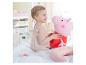 Une jeune fille en robe rose joue avec une peluche Peppa Pig sur un lit avec une housse de couette arc-en-ciel.