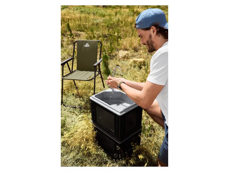 Homme se lavant les mains à un évier portable avec une chaise de camping en arrière-plan.