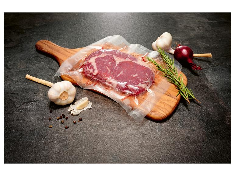 Steak de bœuf sous vide avec ail, oignon rouge et romarin sur une planche en bois.
