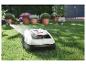 Robot tondeuse lavé au jet d'eau dans un jardin avec des plantes en pot.