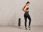 Une femme en leggings noirs et un soutien-gorge de sport se tient à côté d'un tapis de yoga.