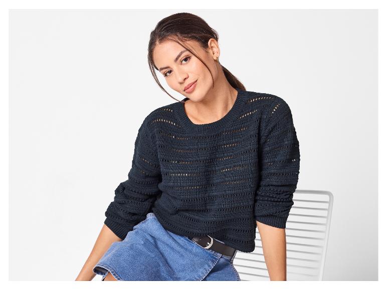 Femme en pull en maille bleu foncé et jupe en jean, assise sur une chaise.