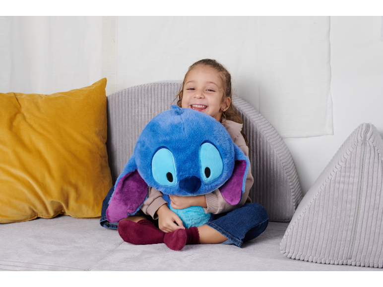 Fille souriante étreint une peluche bleue sur un canapé gris avec des coussins.