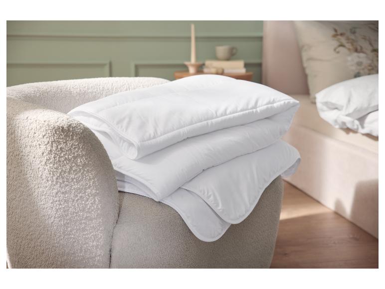 Pile de couettes blanches sur un fauteuil beige dans une chambre.