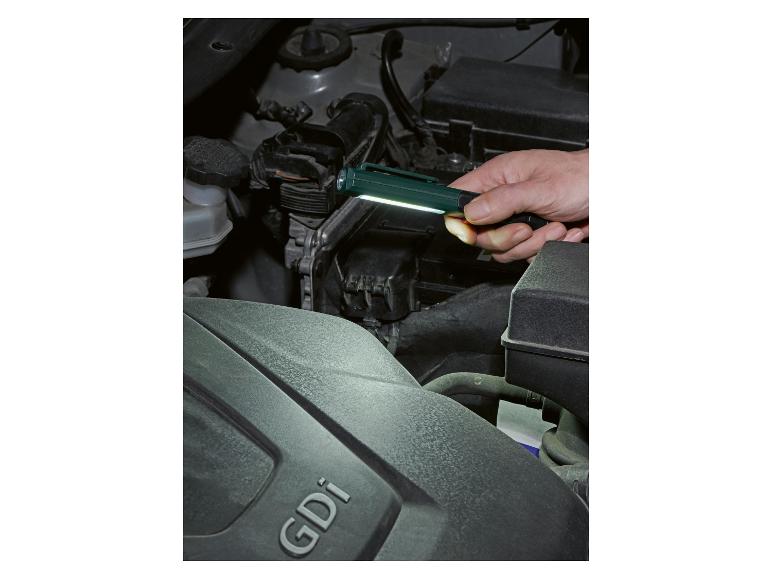 Homme éclairant le moteur d'une voiture avec une lampe de poche, inscription GDi visible.