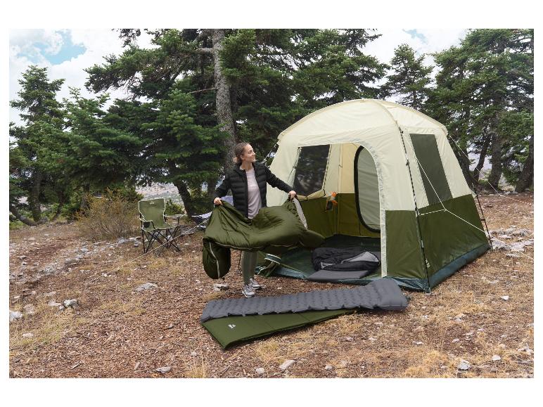 Une femme déplie un sac de couchage vert CRIVIT devant une tente.