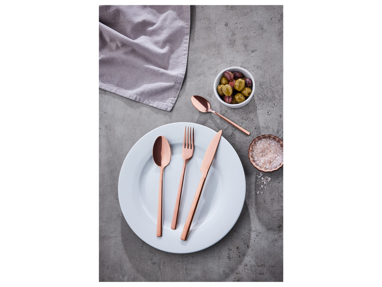 Une fourchette, un couteau et une cuillère en acier inoxydable de couleur cuivre sur une assiette blanche.