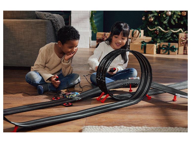 Deux enfants jouent avec une piste de course Carrera avec une voiture de police.