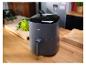 Friteuse à air gris foncé sur un comptoir de cuisine en bois avec des légumes en arrière-plan