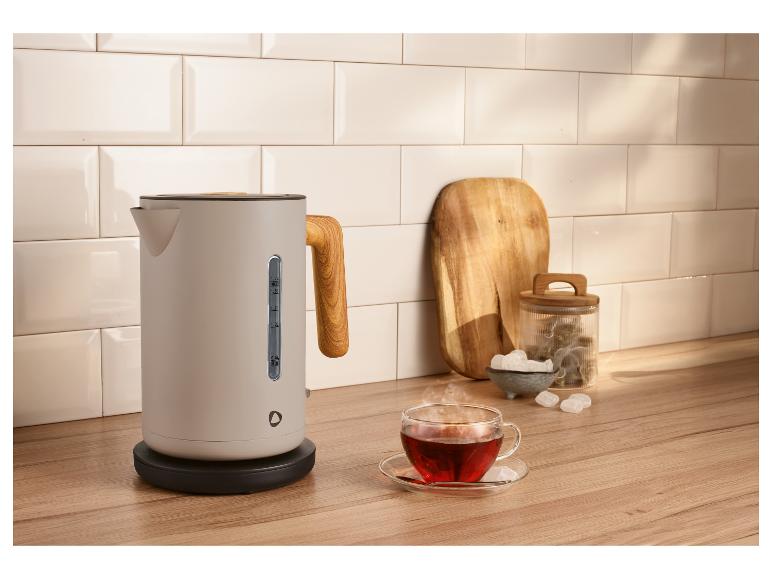 Bouilloire moderne avec poignée en bois, une tasse de thé et accessoires sur un comptoir en bois.