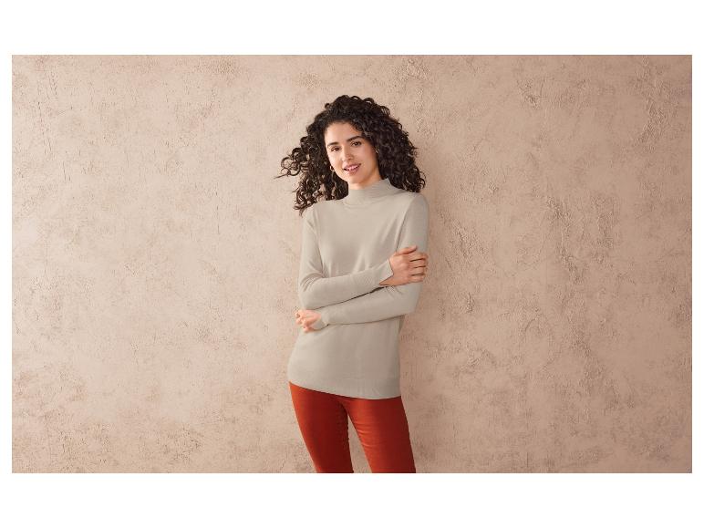 Une femme porte un pull beige et un pantalon rouge.