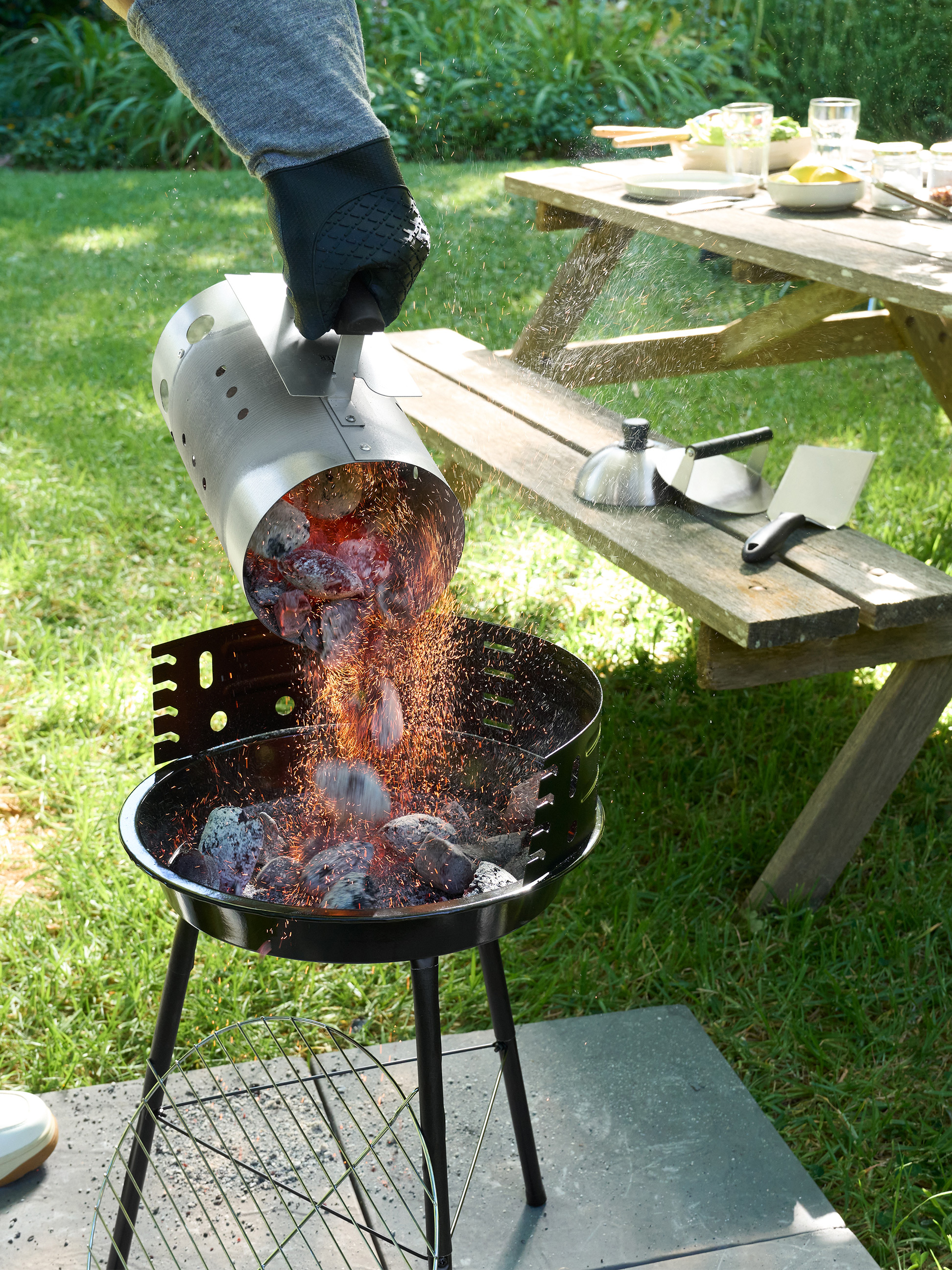 Charbon ardent versé d'une cheminée d'allumage dans un barbecue à charbon dans un jardin.