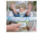 Gros plan d'une main appuyant sur un bouton d'un transat bébé avec un bébé en arrière-plan.