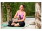 Une femme assise sur un tapis de yoga à côté de ses mules de bain CRIVIT vert clair.
