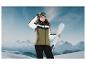 Une femme portant une veste de ski et des lunettes de ski tient des skis sur fond de montagnes.