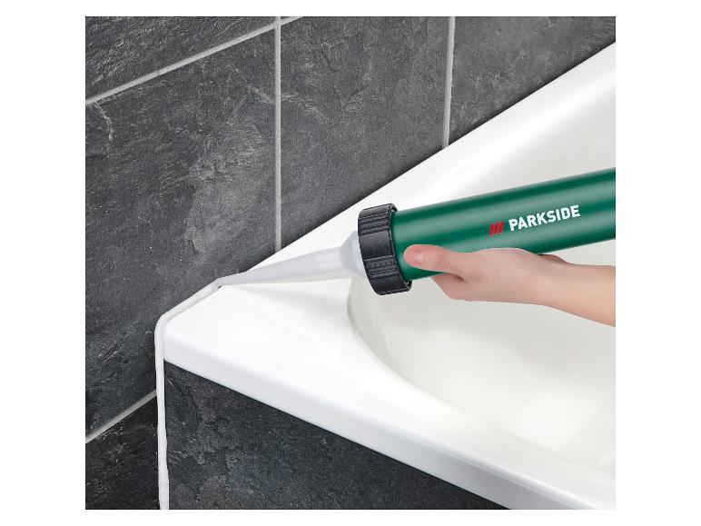 Application de mastic blanc sur le bord d'une baignoire avec un pistolet à calfeutrer.