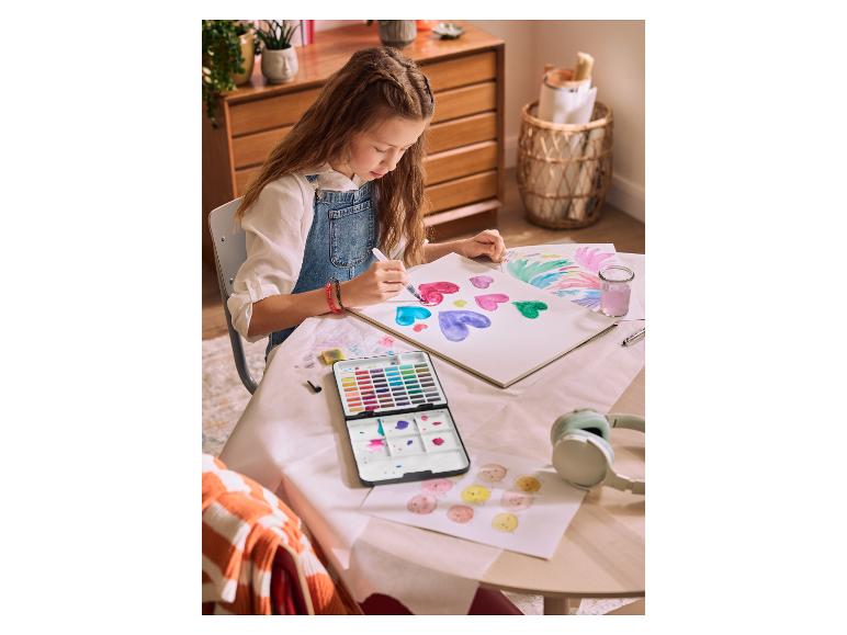 Une fille peint des cœurs colorés à l'aquarelle à une table, avec un casque sur la table.