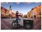 Une femme sur un vélo cargo noir SachsenRAD sur une place de ville.