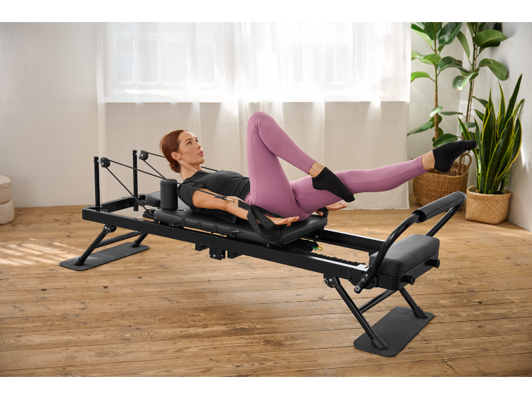 Une femme s'entraînant sur un appareil de pilates reformer noir dans une pièce lumineuse