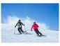 Deux personnes en tenue de ski descendent une pente.