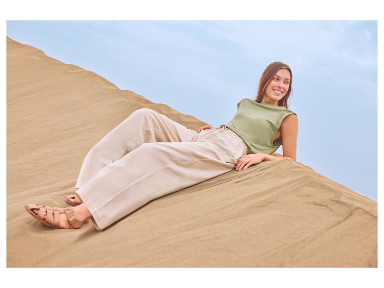 Femme en haut vert et pantalon beige se relaxant sur une dune de sable.