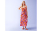 Une femme porte une robe longue rose à imprimé floral et des sandales rouges.