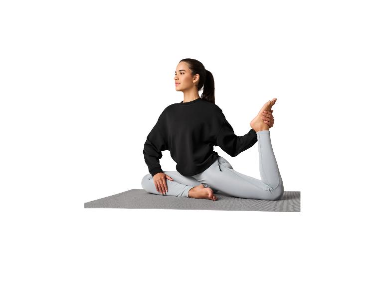Femme en sweat-shirt noir et leggings gris clair sur un tapis de yoga