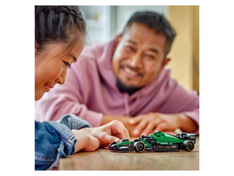 Une fille et un homme jouent avec une voiture de course verte Aston Martin Aramco.