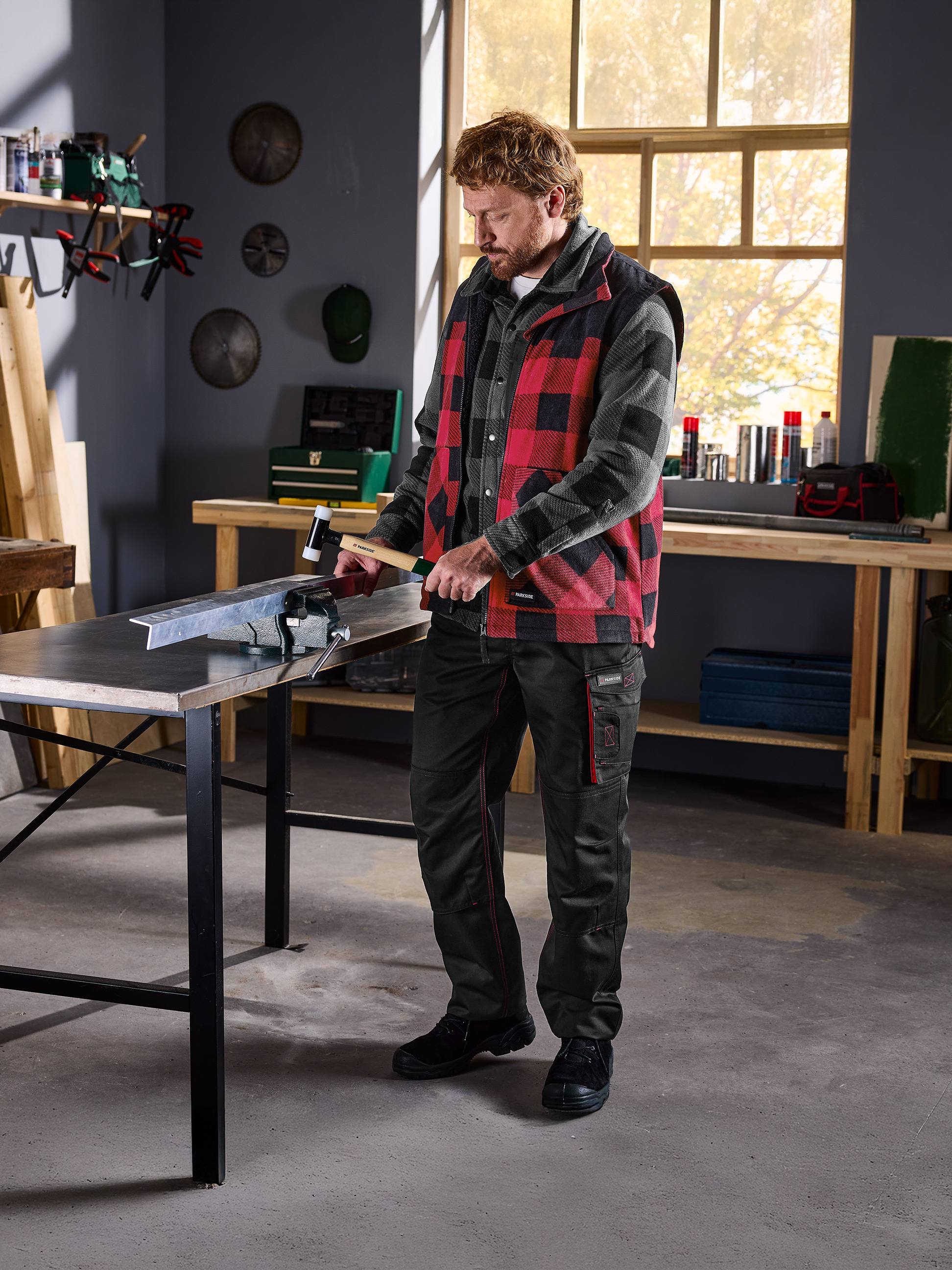 Homme en chemise à carreaux et gilet Parkside travaillant le métal dans un étau en atelier.