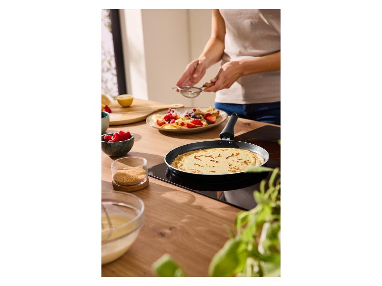 Personne préparant des crêpes aux fruits rouges et au sucre dans une poêle en cuisine.