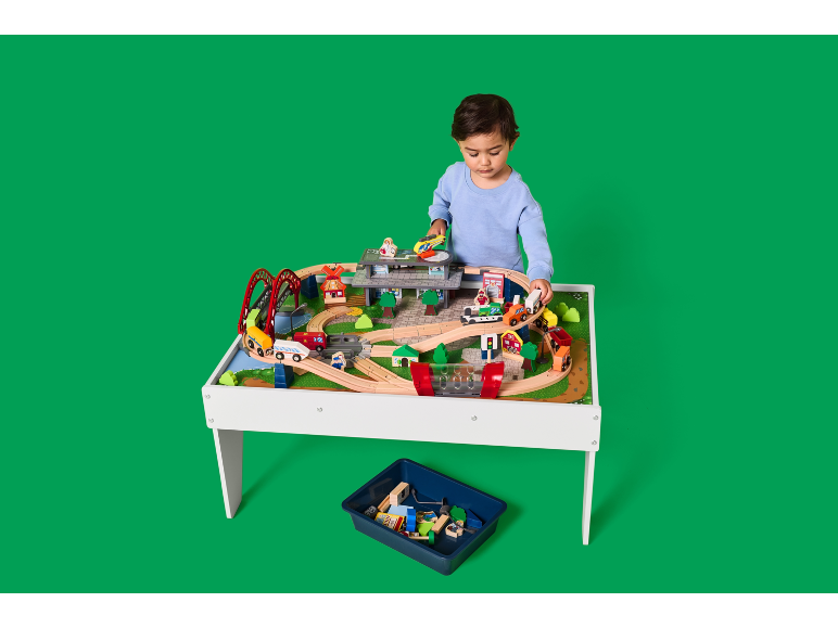 Enfant jouant avec une table de jeu en bois avec train et accessoires.