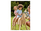 Deux enfants jouent avec un cheval en bois dans le jardin.